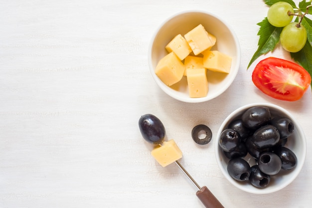 Ingrediënten voor snacks, kaas met olijven en tomaat, druif op een witte tafel