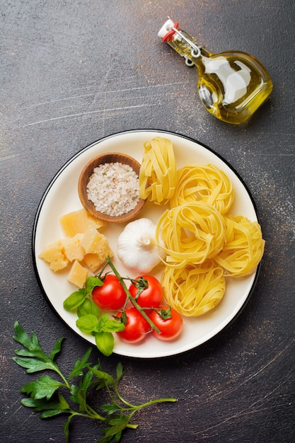 Ingrediënten voor traditionele Italiaanse pastagerecht. Ongekookte rauwe tagliatelle bolognesi, parmezaanse kaas, olijfolie, knoflook, basilicumblaadjes, paprika, kerstomaatjes. Bovenaanzicht