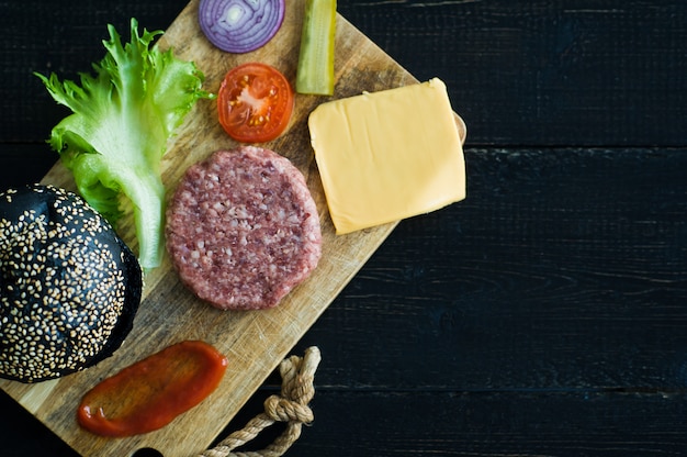 Ingrediënten voor zwarte Hamburger op houten hakbord, zwarte achtergrond.