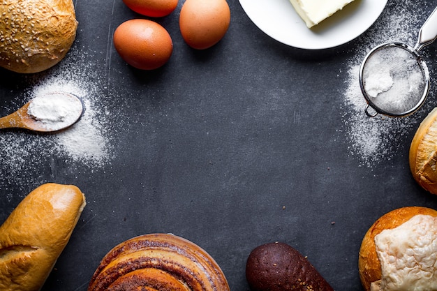 Ingredients for baking bakery products. Fresh homemade crisp bread, baguette, buns on a black chalkboard frame background