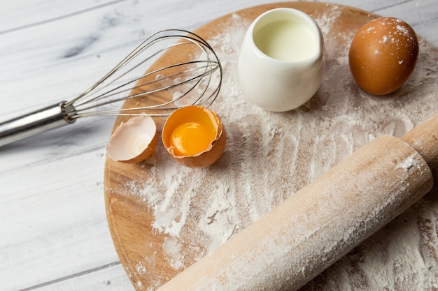 The ingredients for baking on the table are wheat flour on a board eggs milk and a whisk