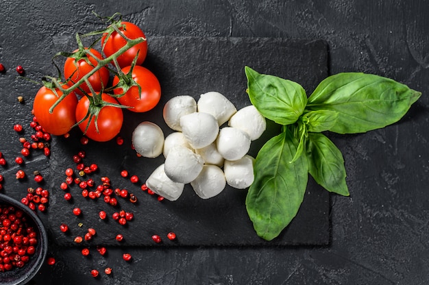 Ingredients for Caprese salad, Mini mozzarella cheese, Basil leaves and cherry tomatoes. black background. top view