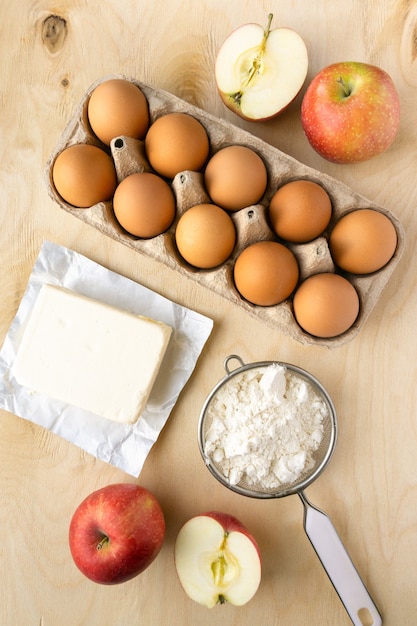 Ingredients for cooking apple pie. Eggs, flour and butter on wooden background, top view