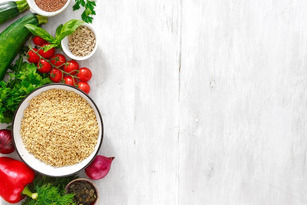 Ingredients for cooking diet and healthy food. green buckwheat, sunflower and flax seeds, vegetables and greens top view on wooden white table 