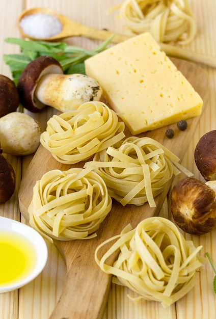 Ingredients for cooking fettuccine pasta with porcini mushrooms and cheese on a wooden background.