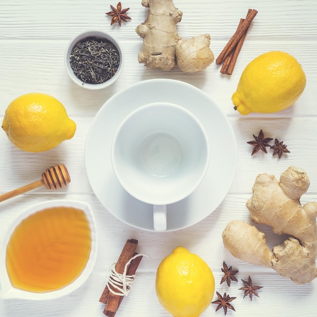 Ингредиенты для приготовления здорового натурального горячего напитка Лимоны, мед, имбирь и корица вокруг пустой чашки