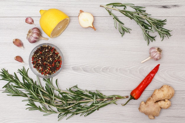 Ingredients for cooking meat or fish. Ginger root, chili pepper, garlic, onion, lemon, allspice peppers in glass bowl and rosemary on a wooden background. Top view with copy space.