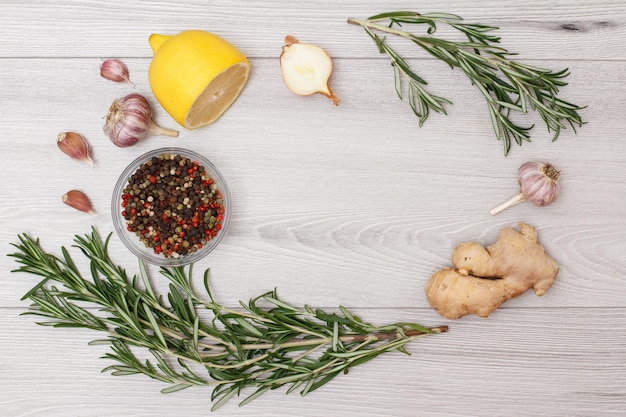 Ingredients for cooking meat or fish. Ginger root, garlic, onion, lemon, allspice peppers in glass bowl and rosemary on a wooden background. Top view with copy space.