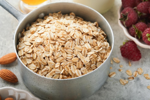 Ingredients for cooking oatmeal or granola with oats milk raspberries honey and almonds on gray concrete old table background Ingredients for healthy breakfast