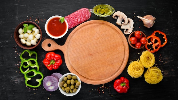 Ingredienti per cucinare la pasta pasta secca funghi salsicce pomodori verdure vista dall'alto su fondo di legno nero spazio libero per la copia