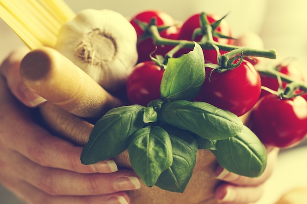 Ingredienti per la cottura della pasta. pomodori, basilico fresco, aglio, spaghetti. cook tiene ingredienti freschi per la cottura. tonificante. messa a fuoco selettiva.