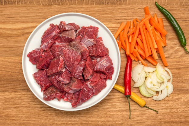 Ingredients for cooking pilaf on a wooden background. Onions, peppers, carrots, minced meat lie on a wooden cutting board. Cooking pilaf at home.