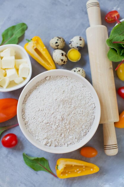 Ingredients for cooking vegetable Fresh colorful vegetables quail eggs butter whole grain flour and rolling pin on a grey background Bakery background