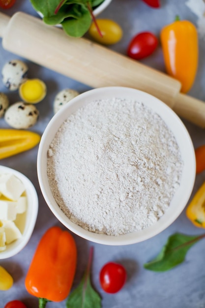 Ingredients for cooking vegetable Fresh colorful vegetables quail eggs butter whole grain flour and rolling pin on a grey background Bakery background