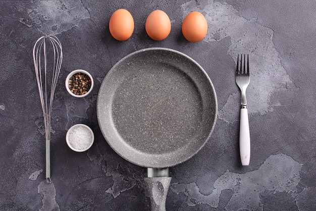 Ingredients and dishes for making scrambled eggs lie on a dark stone background