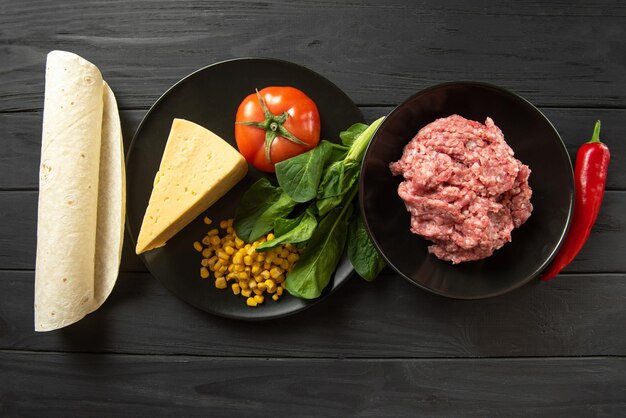 Ingredients for encheladas on a black background meat pita tomato peppers and basil flat lay