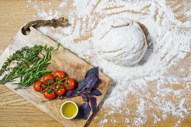 Ingredients for Focaccia: dough, tomatoes, rosemary, thyme, Basil, olive oil on a wooden table. 