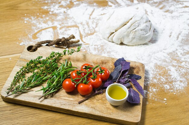 Ingredients for Focaccia: dough, tomatoes, rosemary, thyme, Basil, olive oil on a wooden table. 