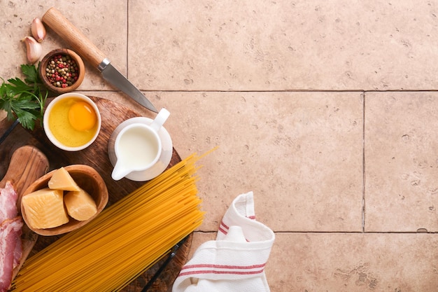 パスタカルボナーラの材料伝統的なイタリアンパスタカルボナーラ材料ベーコンスパゲッティパルメザンチーズと卵黄にんにくベージュ古いタイルテーブルの背景上面図コピースペース
