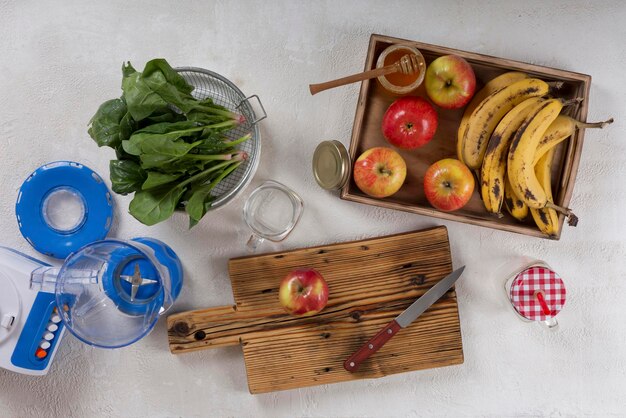 テーブルのクローズアップにほうれん草を添えたフルーツスムージーの材料。バナナ、りんご、ほうれん草、はちみつ