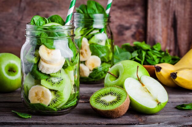 Ingredients for healthy smoothie in glass jar banana kiwi spinach green apple on rustic background