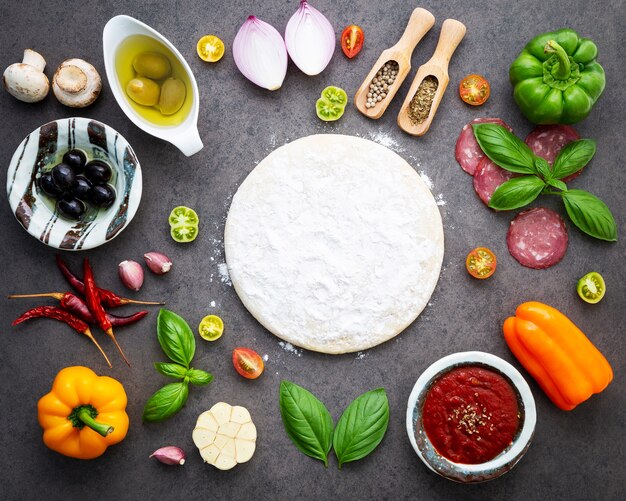 Foto gli ingredienti per la pizza fatta in casa su sfondo scuro di pietra.