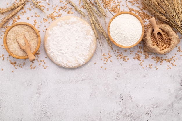 Foto gli ingredienti per l'impasto della pizza fatta in casa con spighe di grano, farina di frumento e chicchi di grano, disposti su fondo di cemento bianco