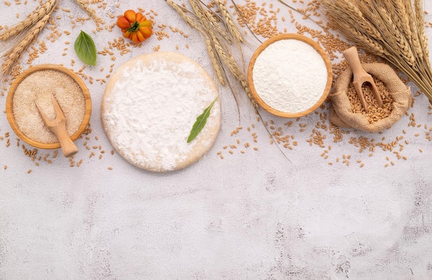 Foto gli ingredienti per l'impasto della pizza fatta in casa con spighe di grano, farina di frumento e chicchi di grano, disposti su fondo di cemento bianco