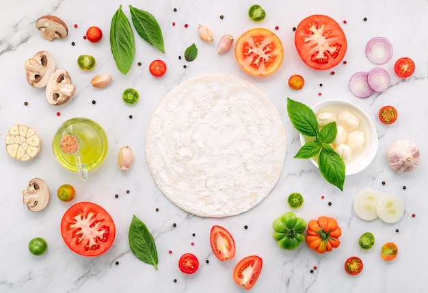 Gli ingredienti per la pizza fatta in casa allestiti su sfondo di marmo bianco.