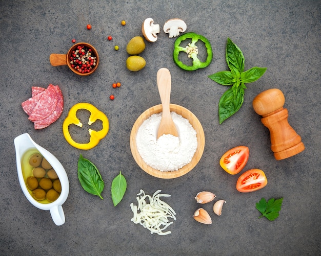 The ingredients for homemade pizza with herbs  flat lay on dark stone background.