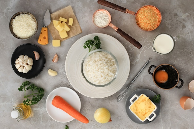 Photo ingredients for making cooking arancini on a white grey marble background. cheese, rice, milk, egg, carrot, parsley, butter, garlic, bread crumb, and parmesan