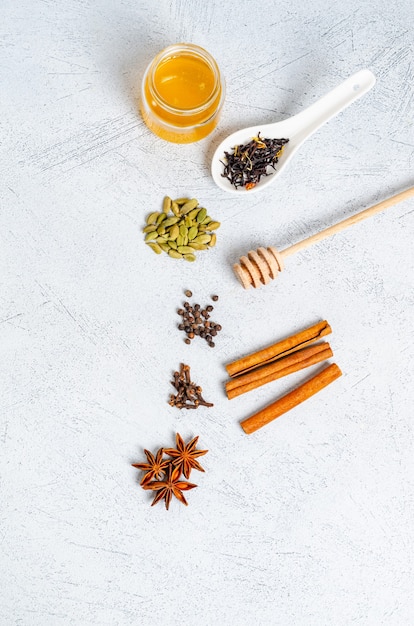 Ingredients for making indian traditional masala tea drink. Cinnamon, cardamom, anise, honey, cloves, dry tea on a light table. View from above. Copy space for text, flat lay.Vertical orientation