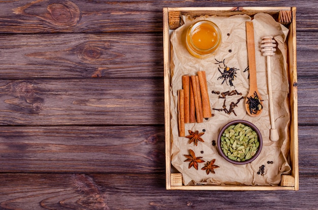 Ingredients for making indian traditional masala tea drink in a wooden tray.