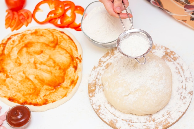 Ingredients for making pizza on a white background. Italian food. The cook sprinkles flour on the dough. Cheese, tomato, pizza dough, flour, sauce, olives and others