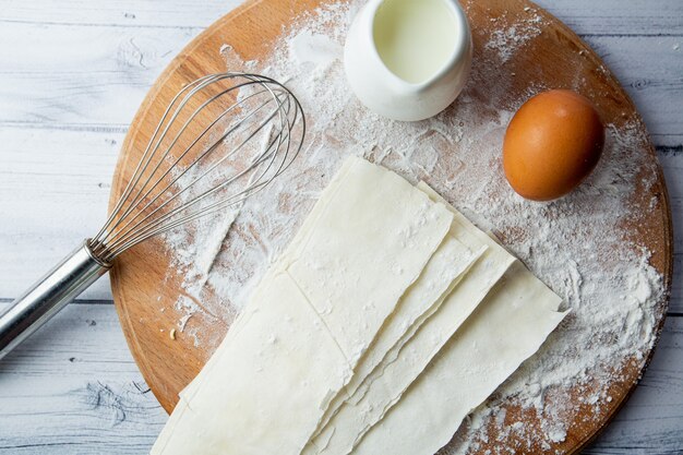 The ingredients for making puff pastry on the table are puff pastry plates eggs milk and a whisk view from above