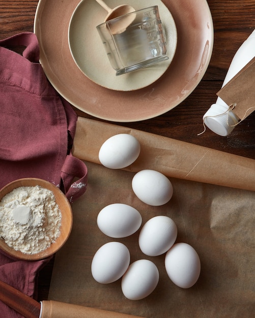 Ингредиенты для блинов и пирогов на деревянном столе с посудой и бумагой для выпечки, плоская форма