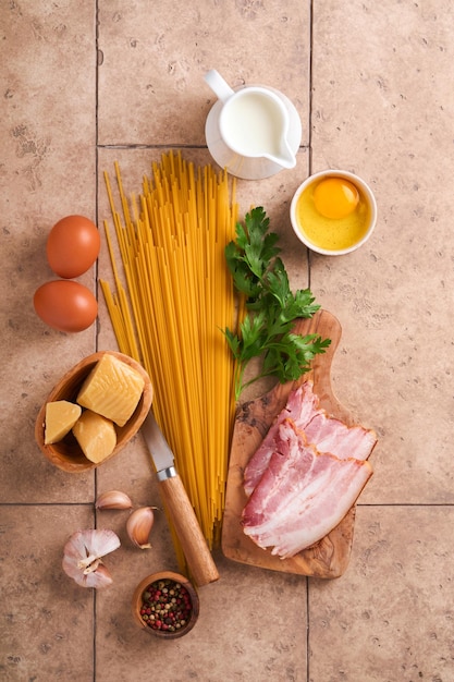 Ingredients for pasta carbonara traidtional italian pasta\
carbonara ingredients bacon spaghetti parmesan and egg yolk garlic\
beige old tile table background top view copy space