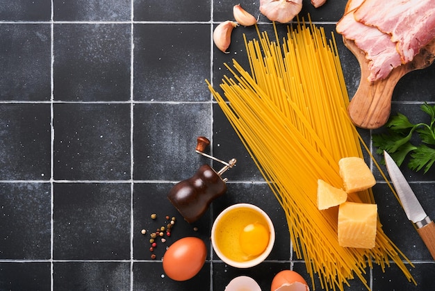 パスタカルボナーラの材料伝統的なイタリアンパスタカルボナーラ材料ベーコンスパゲッティパルメザンチーズと卵黄にんにく黒の古いタイルテーブルの背景上面図コピースペース
