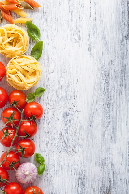 Struttura del basilico dei pomodori della pasta degli ingredienti su legno bianco