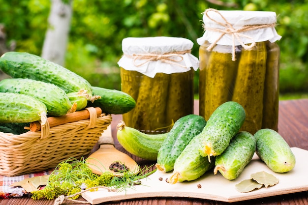 Ingredients for pickling cucumbers on a wooden table in the background of the garden. Cucumbers, dill, pepper and bay leaf. Glass jars with pickles