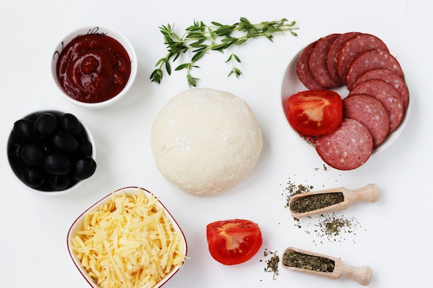 Foto ingredienti per la pizza: pasta, salsiccia, pomodori, olive, salsa di pomodoro, formaggio, basilico ed erbe di provenza