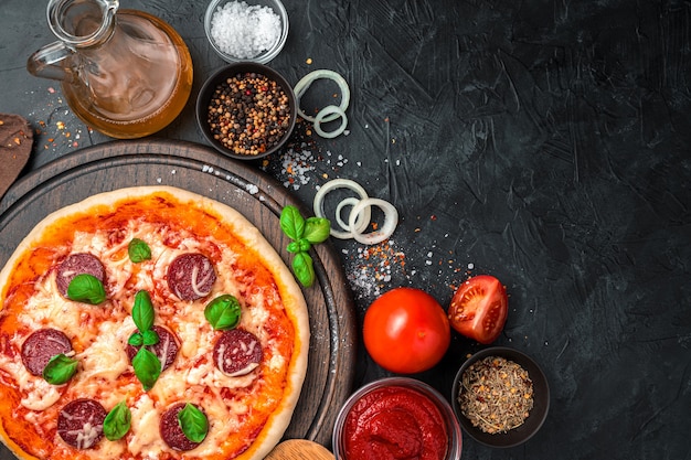 Ingredients and ready-made pizza on a concrete black background