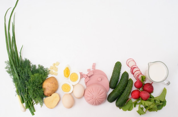 Ingredienti per la minestra fredda russa nazionale di okroshka su uno sfondo chiaro. patate, ravanelli, salsiccia, cipolle, erbe, uova. la vista dall'alto