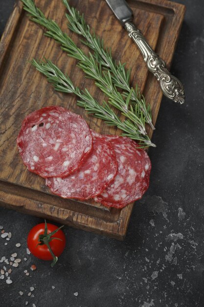 Ingredients for sandwich, Sausage on wooden board with rosemary, vintage knife and bread with tomatoes on black stone background, Top View