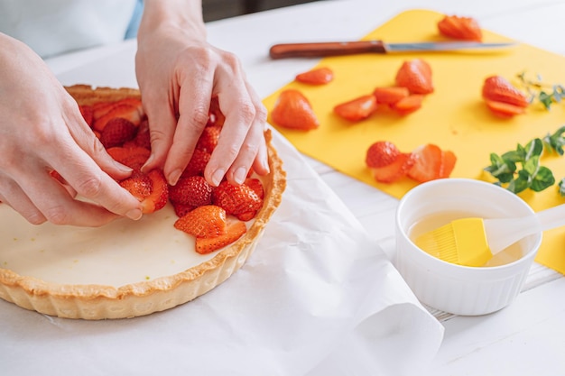ストロベリーパイカスタードケーキとライムゼストまな板とスライスしたイチゴの材料女性の手はスライスしたイチゴをクリームの表面に置きます