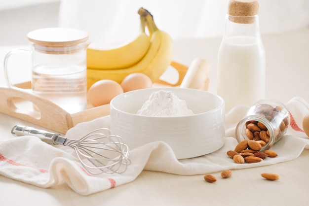 Ingredients and tools to make banana cake on white surface