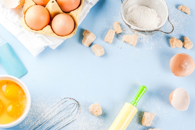 Ingredients and utensils for cooking baking egg, flour, sugar, whisk, rolling pin, on blue background, top view