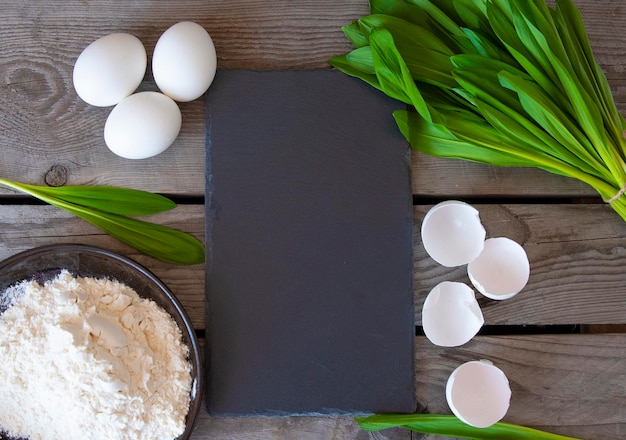 Ingredients for wild garlic pies and a black board to write down the recipe Wooden background