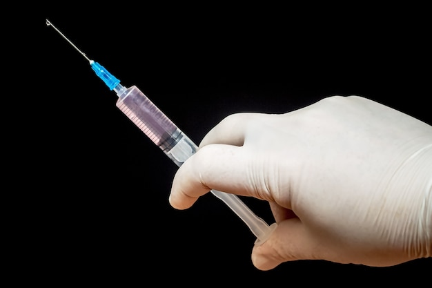 Injection syringe in doctor's hand on black isolated background