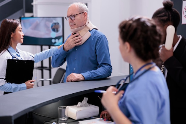 Injured elderly patient with cervical neck collar discussing with traumatologist asking for painkillers in hospital waiting room. Old person with medical foam waiting to attend checkup consultation